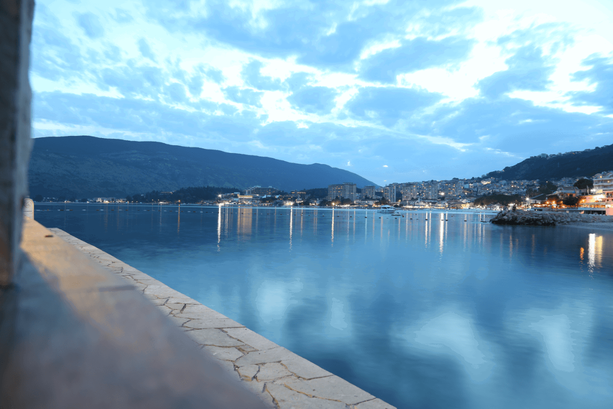 A twilight photo of a harbour with lights in the distance